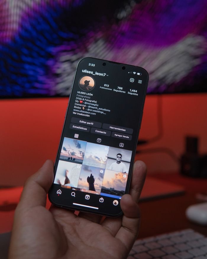 Close-up of a smartphone displaying a social media profile in a warm indoor setting.