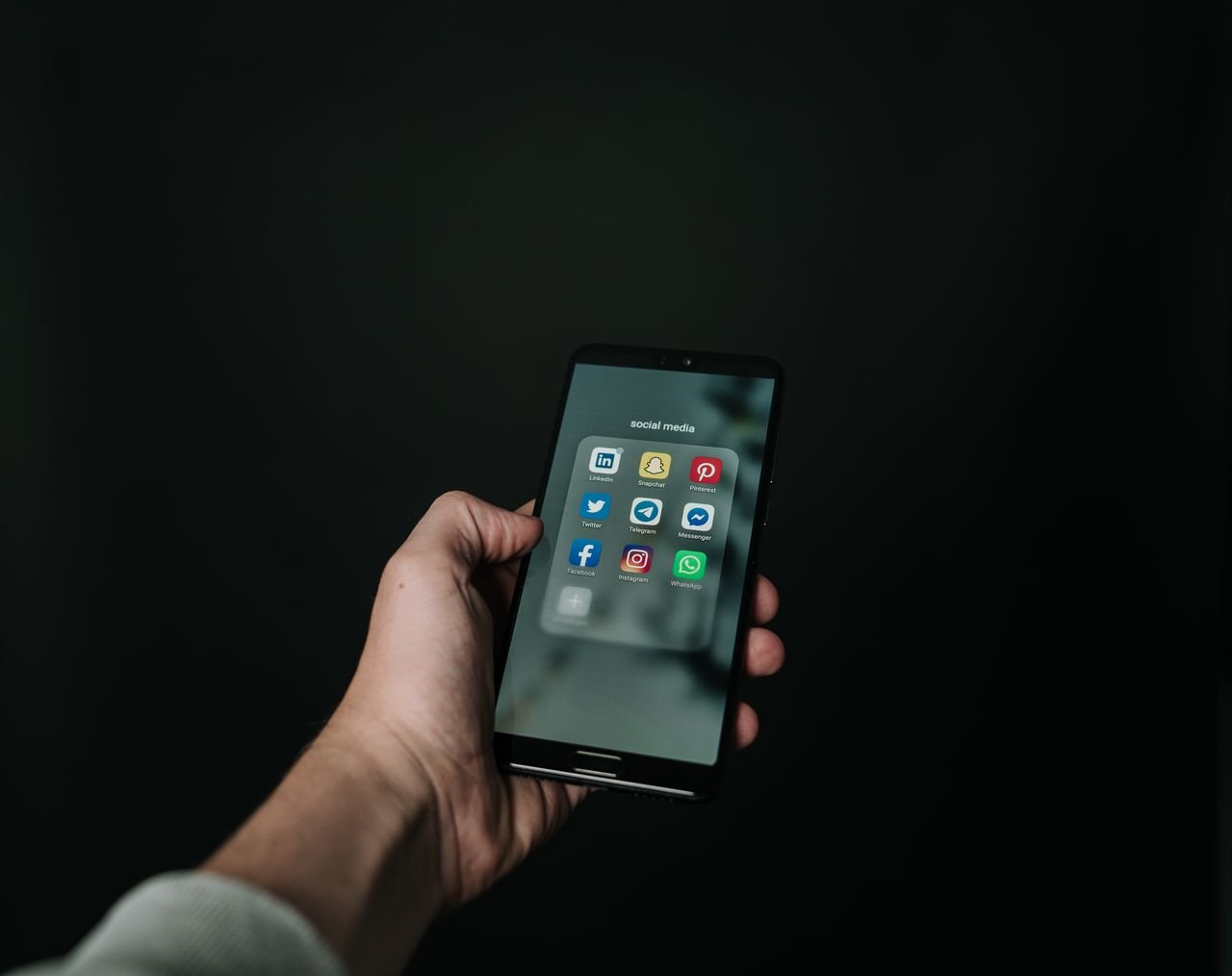 Mastering the First Impression: Your intriguing post title goes here Close-up of a hand holding a smartphone displaying various social media app icons on a dark background.