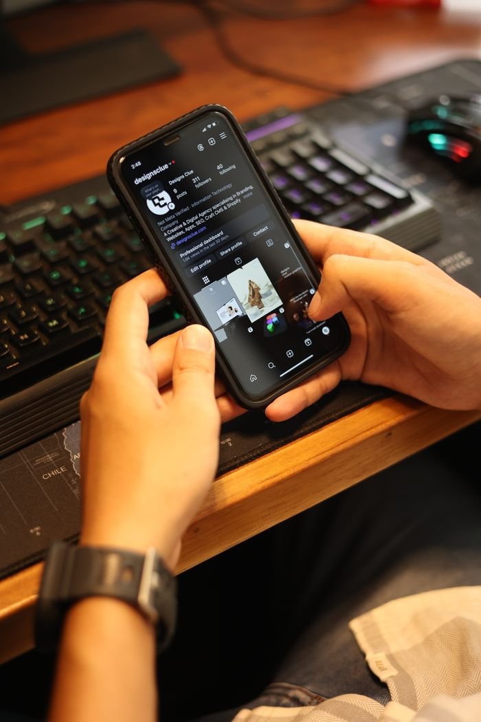 A person using a smartphone to browse a social media app in a tech-themed setup.