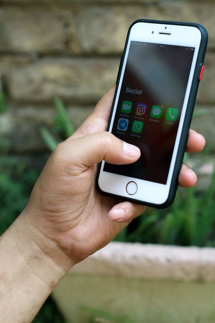Home A person holding a smartphone with social media apps visible, set against a natural backdrop.